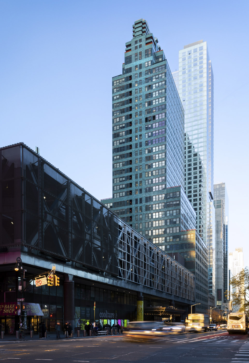 A photograph of a tall blue-green skyscraper taken from street level. The face perpendicular with the street is most visible, and the profile of the building is set back in steps as it rises. A row of small windows runs from bottom to top in the center of the facade. Off of this central core extend horizontal bands of windows separated by teal terracotta areas. The windows wrap around the corners of the building and no corner column or support is visible.